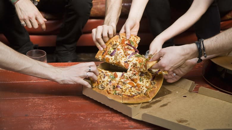 hands grabbing pizza slices