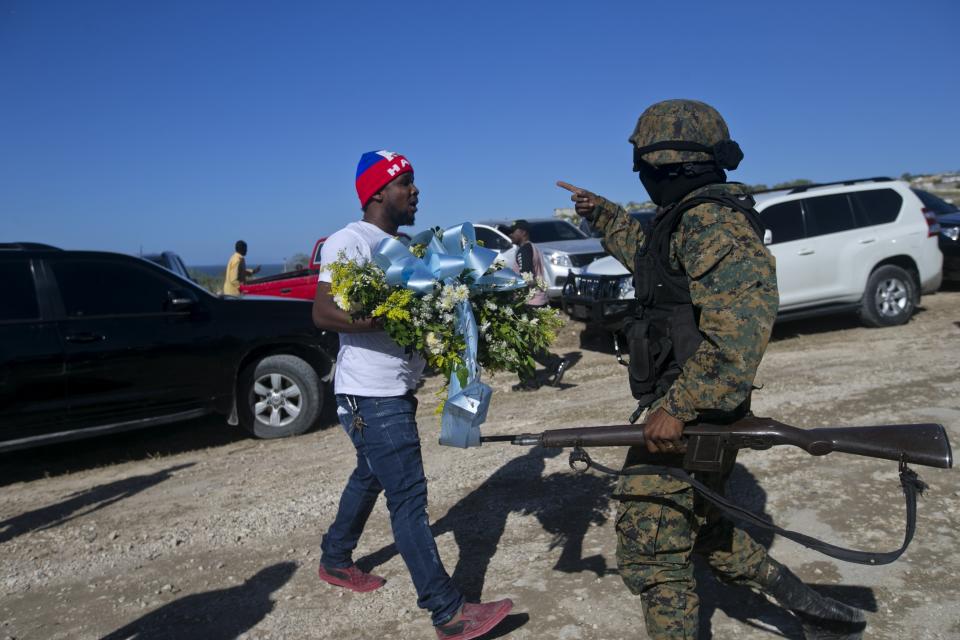 A national police officer stops a man who tries to place flowers at Titanyen, a mass burial site, as Haiti's President Jovenel Moise attends a memorial service honoring the victims of the 2010 earthquake in Port-au-Prince, Haiti, Sunday, Jan. 12, 2020. Sunday marks the 10th anniversary of the devastating 7.0 magnitude earthquake that destroyed an estimated 100,000 homes across the capital and southern Haiti, including some of the country's most iconic structures. (AP Photo/Dieu Nalio Chery)