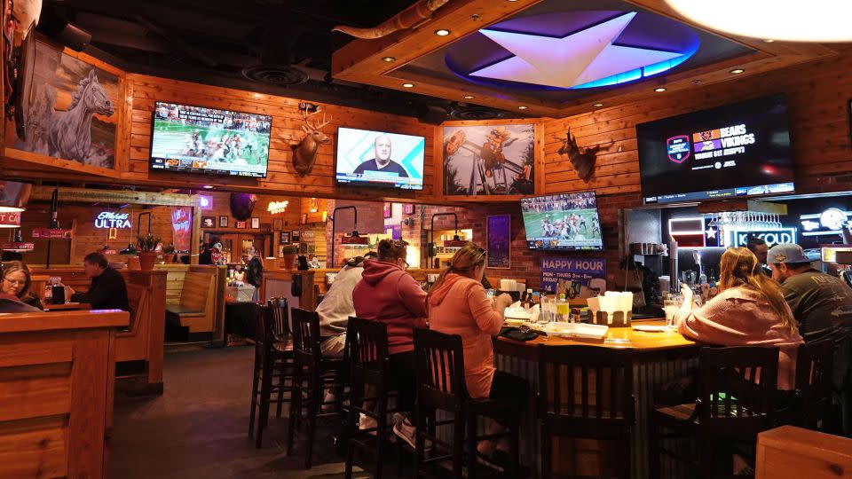 Patrons sit at a bar and watch sports at a Texas Roadhouse restaurant in November 2023. - Hum Images/Alamy Stock Photo