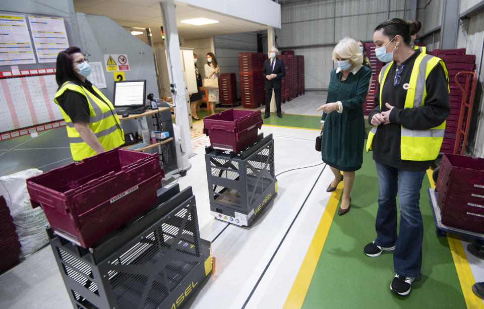 UCKFIELD, UNITED KINGDOM - MARCH 30: Camilla, Duchess of Cornwall is shown around the warehouse by Warehouse staff Zoe Hough and Jenny Milton as she thanks unsung frontline workers during a visit to Kamsons Pharmacy head office and warehouse on March 30, 2021 in Uckfield, East Sussex, United Kingdom. (Photo by Eddie Mulholland-WPA Pool/Getty Images)