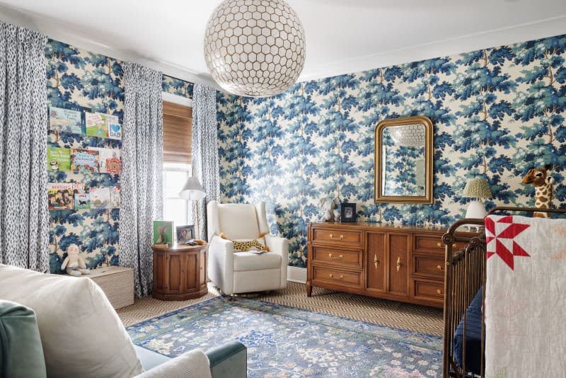 nursery with blue tree wallpaper, blue patterned rug, and vintage furniture
