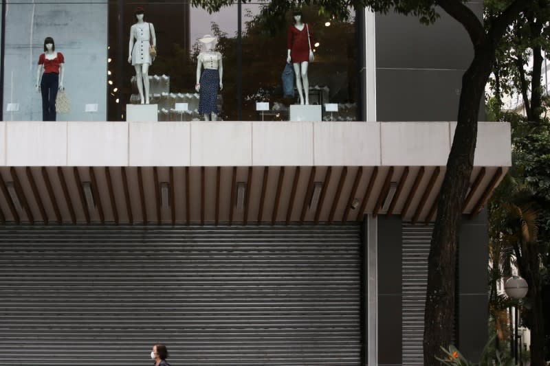 A woman wearing a face mask passes by a closed mall that reduced its opening hours amid the coronavirus disease (COVID-19) outbreak in Sao Paulo