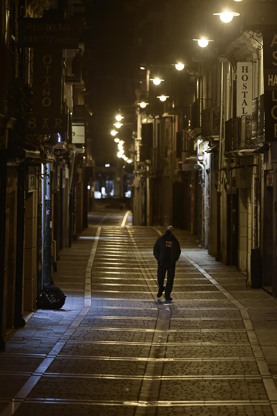 A resident wearing face mask protection walks along an empty San Nicolas street, in Pamplona, northern Spain, Saturday, Oct. 24, 2020, as new measures against the coronavirus began in the Navarra province where all bar and restaurants are closed for 15 days from midnight Wednesday. (AP Photo/Alvaro Barrientos)