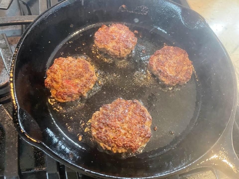 Four browned sliders cooking on a greased black skillet