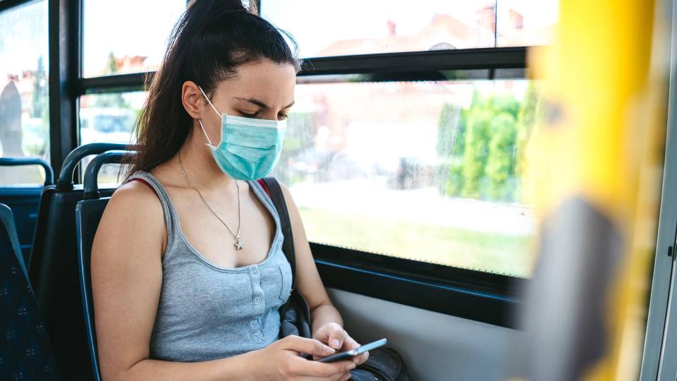 Young caucasian beautiful woman with medical mask taking a bus ride and using her phone while riding.