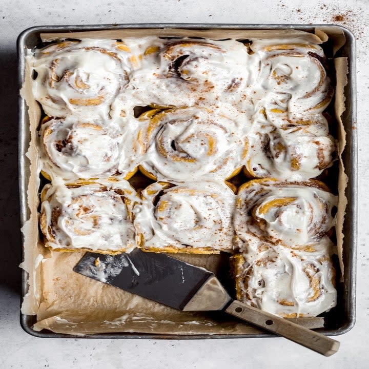 Pumpkin cinnamon rolls with frosting on a baking sheet.