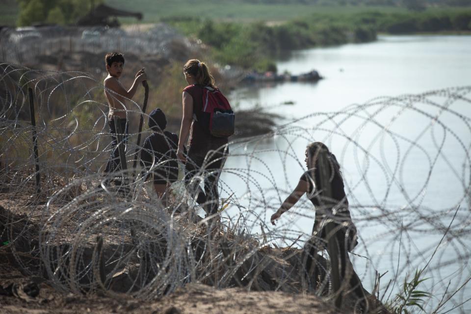 Migrants travel along a steep embankment Saturday searching for an opening in razor wire along the Rio Grande near Eagle Pass.