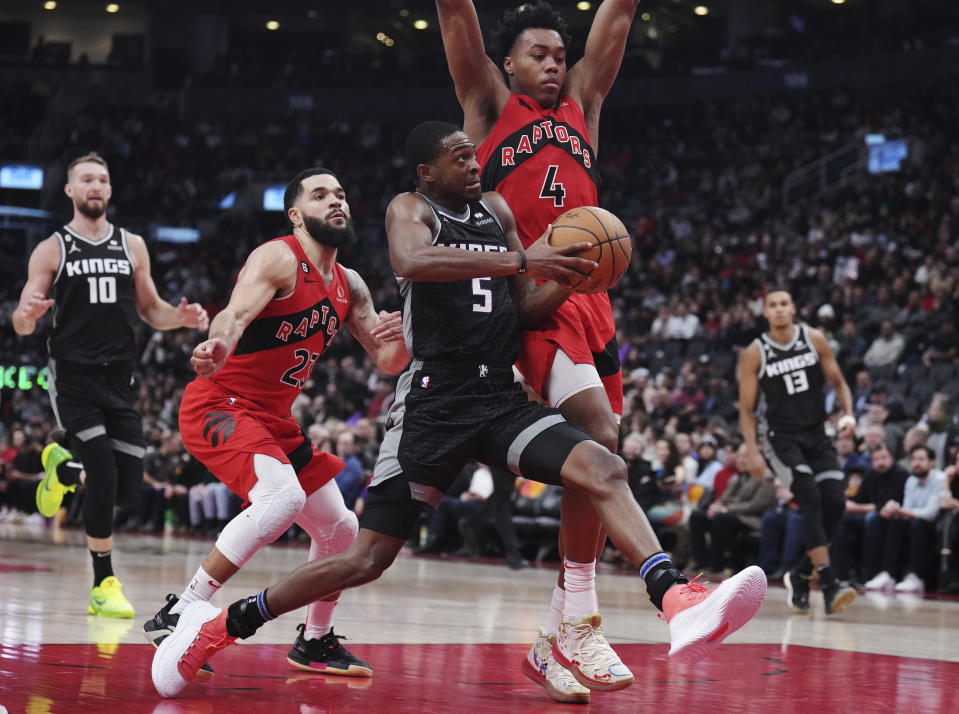 Sacramento Kings guard De'Aaron Fox (5) drives as Toronto Raptors guard Fred VanVleet (23) and forward Scottie Barnes (4) defend during the second half of an NBA basketball game in Toronto on Wednesday, Dec. 14, 2022. (Nathan Denette/The Canadian Press via AP)