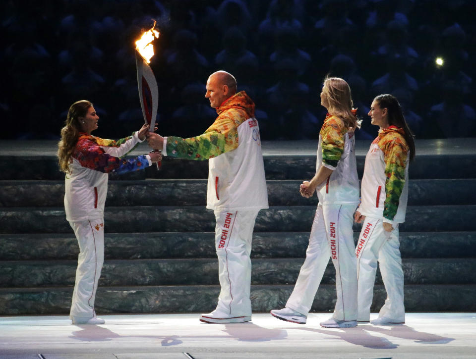 Russian wrestler Alexander Karelin, second from left, hands the torch to Russian gymnast Alina Kabaeva, left, as Russian tennis player Maria Sharapova, second from right, and Russian pole vaulter Yelena Isinbayeva look on during the opening ceremony of the 2014 Winter Olympics in Sochi, Russia, Friday, Feb. 7, 2014. (AP Photo/Mark Humphrey)