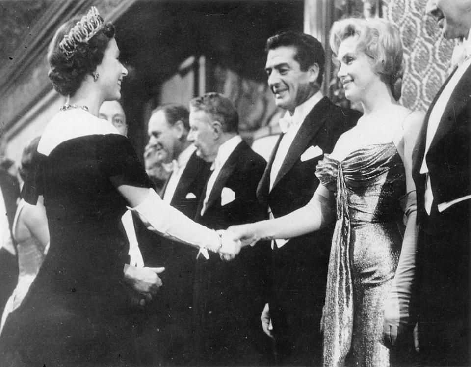 Queen Elizabeth II shakes hands with Marilyn Monroe while Laurence Olivier looks on, all dressed in formal attire at a historical event