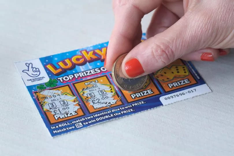 Woman scratching a Lucky Roll scratch card with a British one pound coin (£1). England, UK.