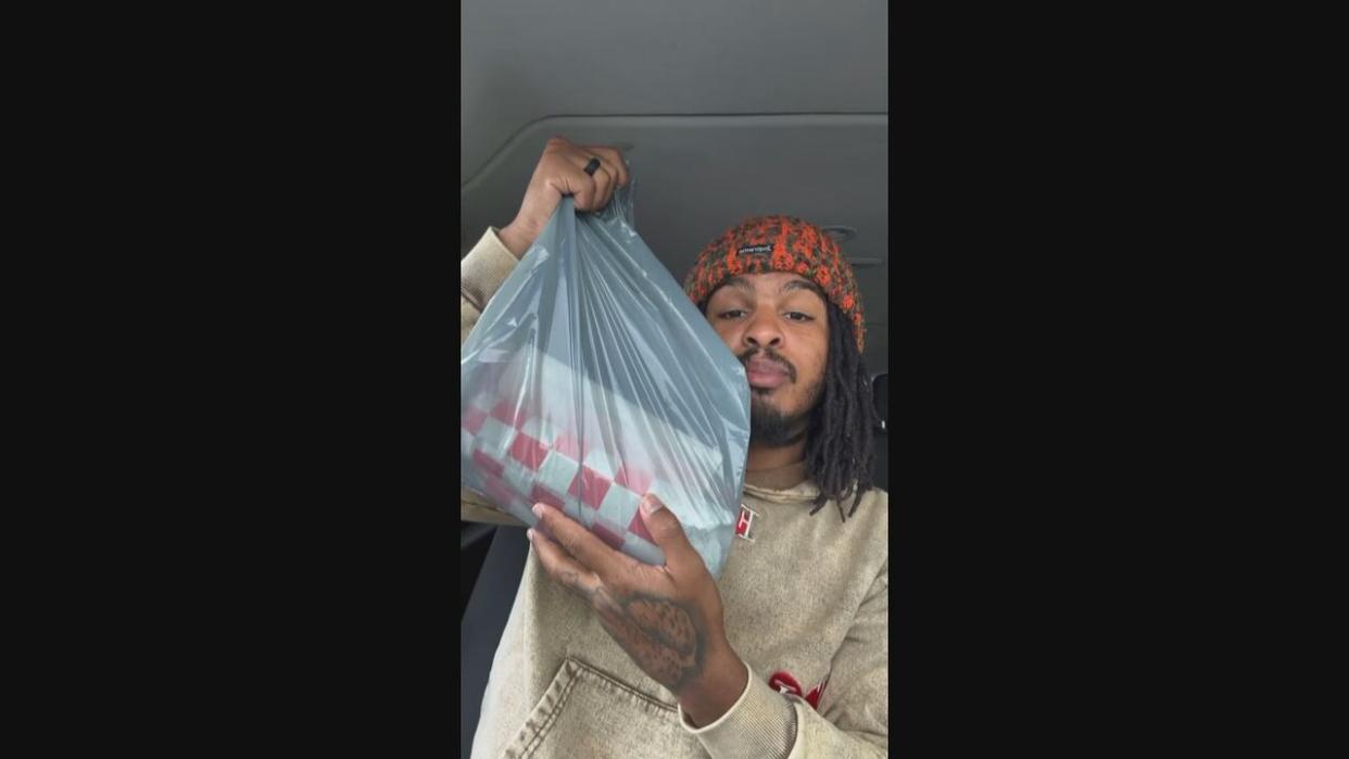 TikTok food critic Keith Lee holds up shawarma from Sumaq Iraqi Charcoal Grill in Scarborough in an image taken from a review posted to TikTok. (CBC - image credit)