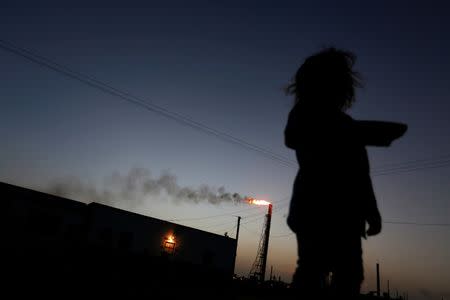 A child stands in front of her house as the Cardon refinery, which belongs to the Venezuelan state oil company PDVSA, is seen in the background in Punto Fijo, Venezuela July 22, 2016. REUTERS/Carlos Jasso