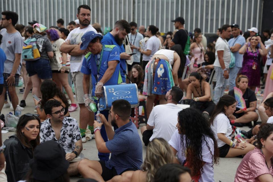 A worker distributes water to fans in Rio de Janeiro waiting for Ms Swift’s Eras Tour on 20 November (Ricardo Moraes/Reuters)