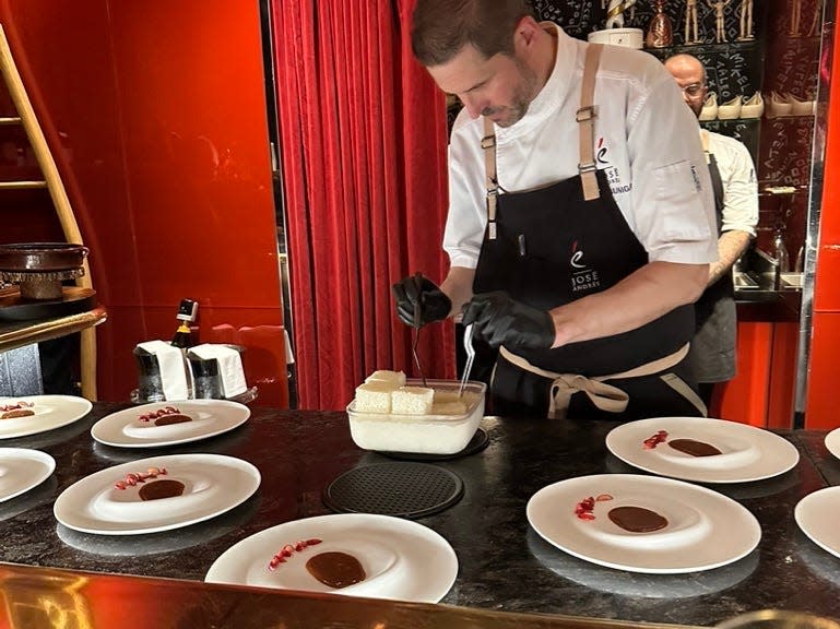 Chef with gloves on preparing small pieces of cake on plates with sauce plated on them