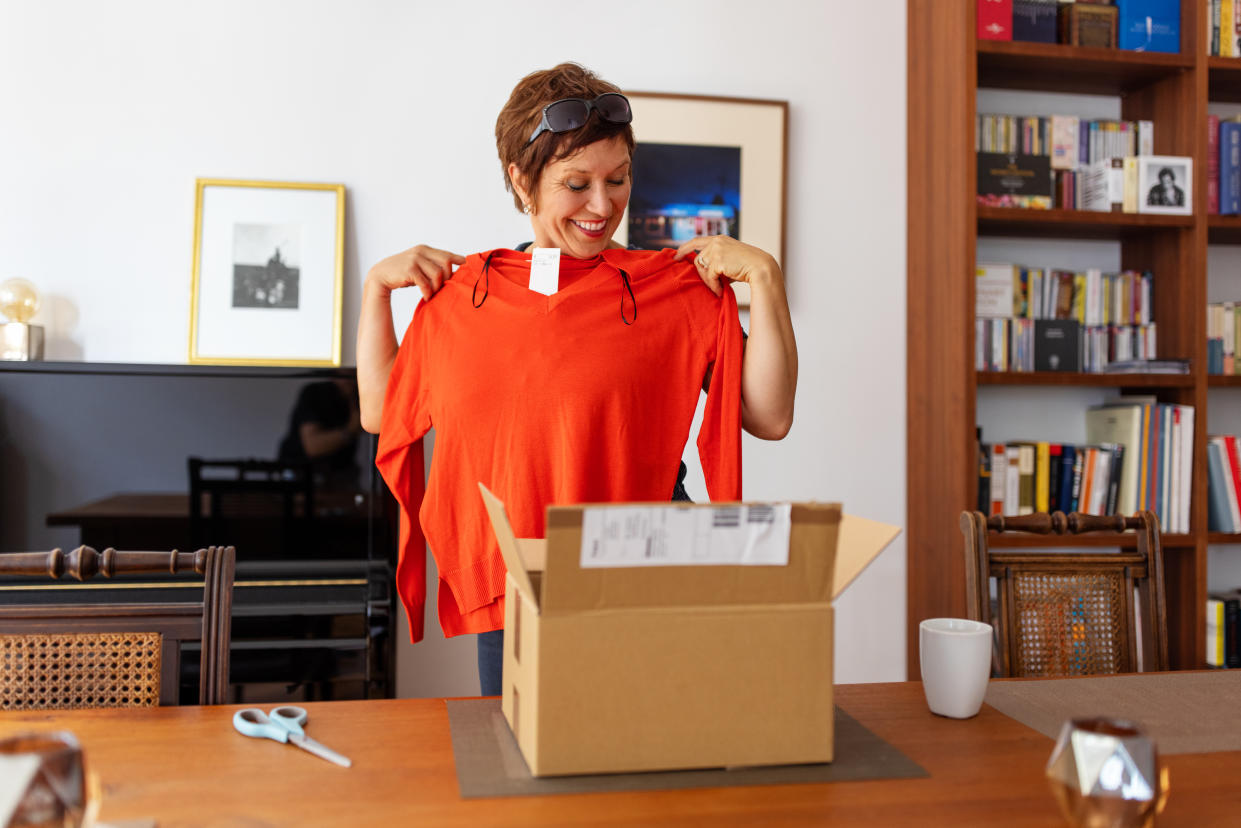 Woman holding up sweater with tags after opening it from the box