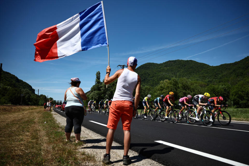 A spectator holding a French national flag along the race route looks on as a lead breakaway cycles past during the 13th stage of the 110th edition of the Tour de France cycling race, 138 km between Chatillon-sur-Chalaronne in central-eastern France and Grand Colombier, in the Jura mountains, in France, on July 14, 2023. (Photo by Anne-Christine POUJOULAT / AFP)