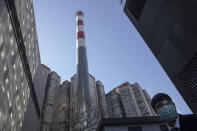 In this photo taken Saturday, Feb. 22, 2020, a security guard looks out near a smoke stack near residential apartments in Beijing, China. Regulators on Monday promised tax cuts and other aid to help companies recover from China's virus outbreak and expressed confidence the ruling Communist Party's growth targets can be achieved despite anti-disease controls that shut down much of the economy. (AP Photo/Ng Han Guan)