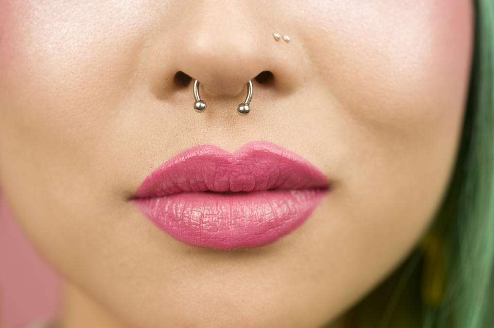 Close-up of a person's lips slightly parted, wearing pink lipstick and a septum nose piercing