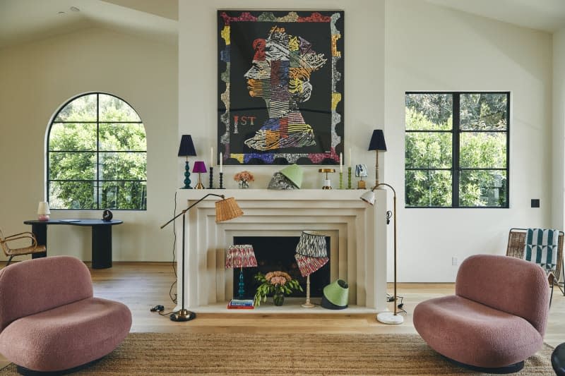 Pink boucle sofas, modern layered fireplace, many patterned and colorful mis matched lamps, geometric portrait art above mantle