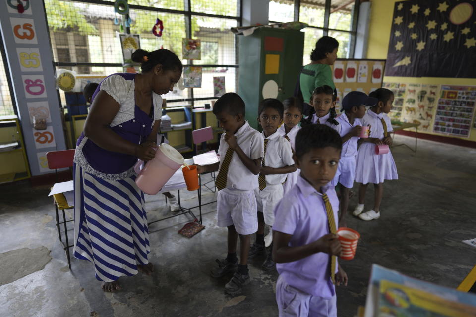 Primary students receive a cup of fresh milk at a Primary School in Dimbulagala, about 200 kilometres north east of Colombo, Sri Lanka, Monday, Dec. 12, 2022. Due to Sri Lanka's current economic crisis in Dimbulagala primary school children receive a free breakfast, a glass of milk and lunch with help from the education ministry, WFP and a private donor agency. Mothers of students prepare the meals at school with the menu provided by the education ministry. Each meal costs $0.27. (AP Photo/Eranga Jayawardena)