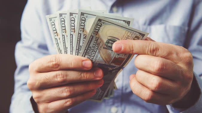 hands counting dollar banknotes on dark wooden surface.