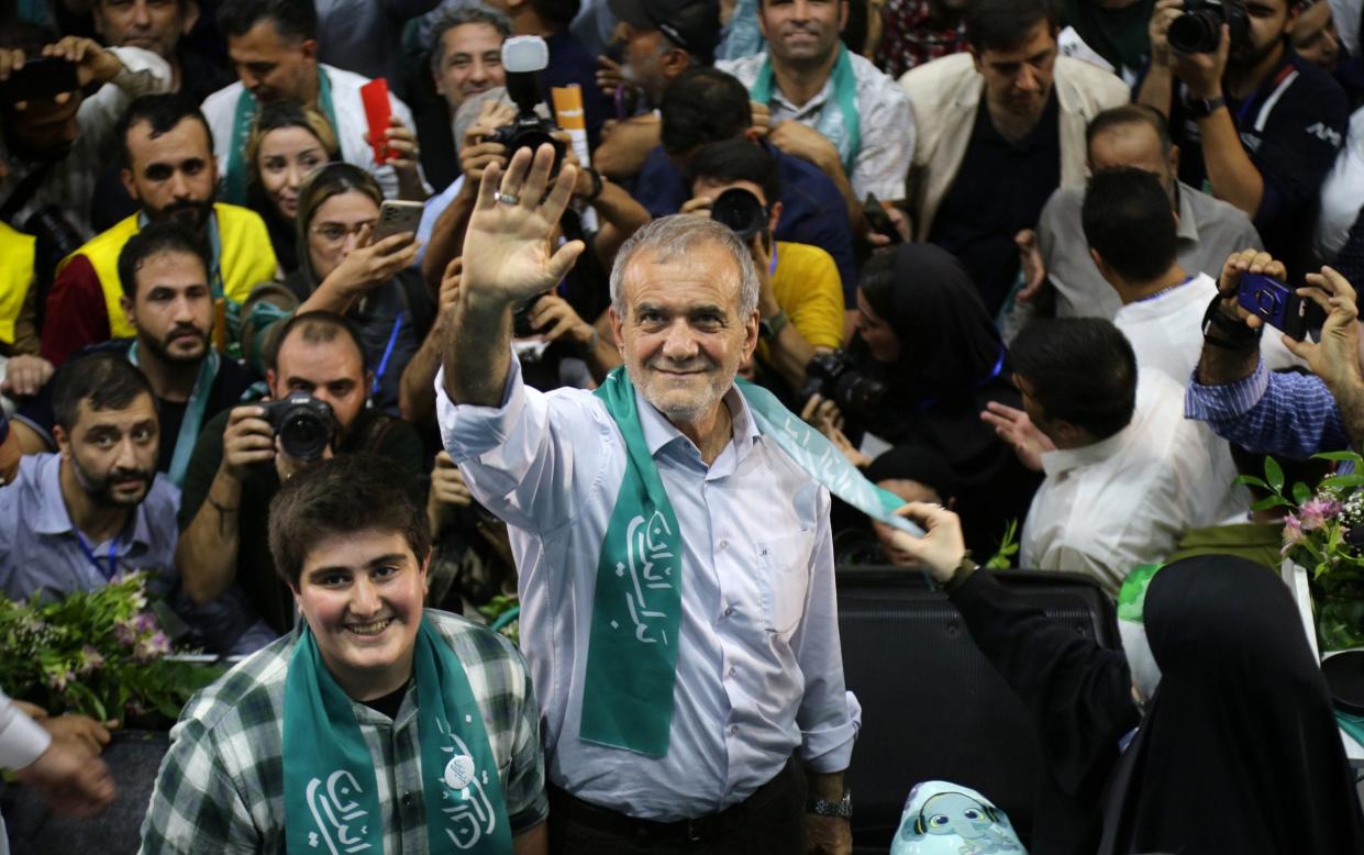 Mr Pezeshkian is seen from a high angle, waving directly into the camera and surrounded by photographers and others