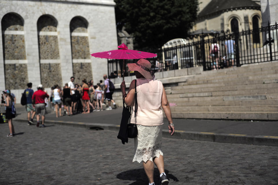 A tourist shelters under an umbrella Wednesday, June 26, 2019 in the Montmartre district of Paris. More than half of France is on alert for high temperatures and the hot weather is expected to last until the end of the week. (AP Photo/Kamil Zihnioglu)