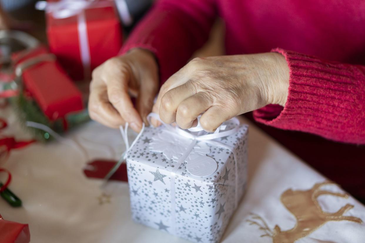 Tying a Christmas ribbon onto a gift to decorate it, a pair of hands performing the intricate knots