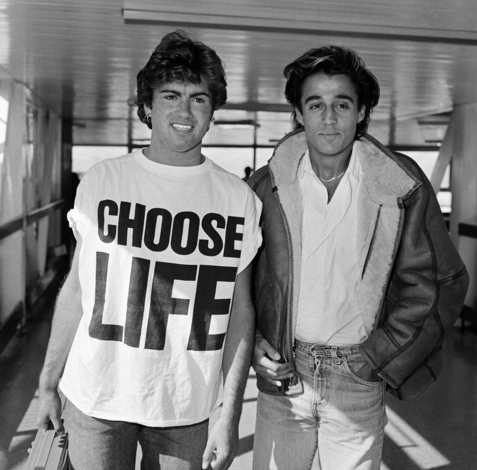 Andrew Ridgeley and George Michael of the pop group Wham!, arriving at London airport. George Michael is wearing a 'Choose Life' t-shirt and holding a portable stereo. 24th May 1984. (Photo by Victor Crawshaw/Mirrorpix/Getty Images)