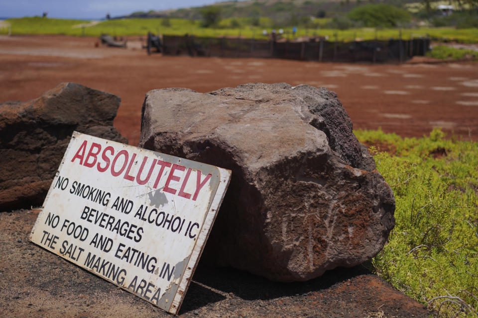A sign and large boulders mark the edge of the Hanapepe salt patch near Salt Pond Beach Park on Wednesday, July 12, 2023, in Hanapepe, Hawaii. Over the past decade, this tract has been under constant threat due to development, pollution from a neighboring airfield, sand erosion from vehicle traffic and littering by visitors to the adjacent beach. (AP Photo/Jessie Wardarski)
