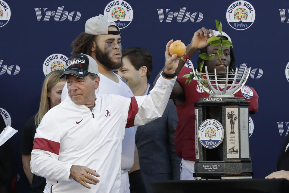 Alabama head coach Nick Saban, left, tosses citrus fruit to his players as they celebrate their victory over Michigan in the Citrus Bowl NCAA college football game, Wednesday, Jan. 1, 2020, in Orlando, Fla. (AP Photo/John Raoux)