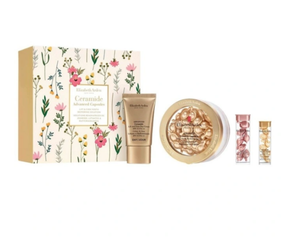 A white and floral box with a gold moisturiser in a tube next to gold and pink tablets in a bottle against a white background.