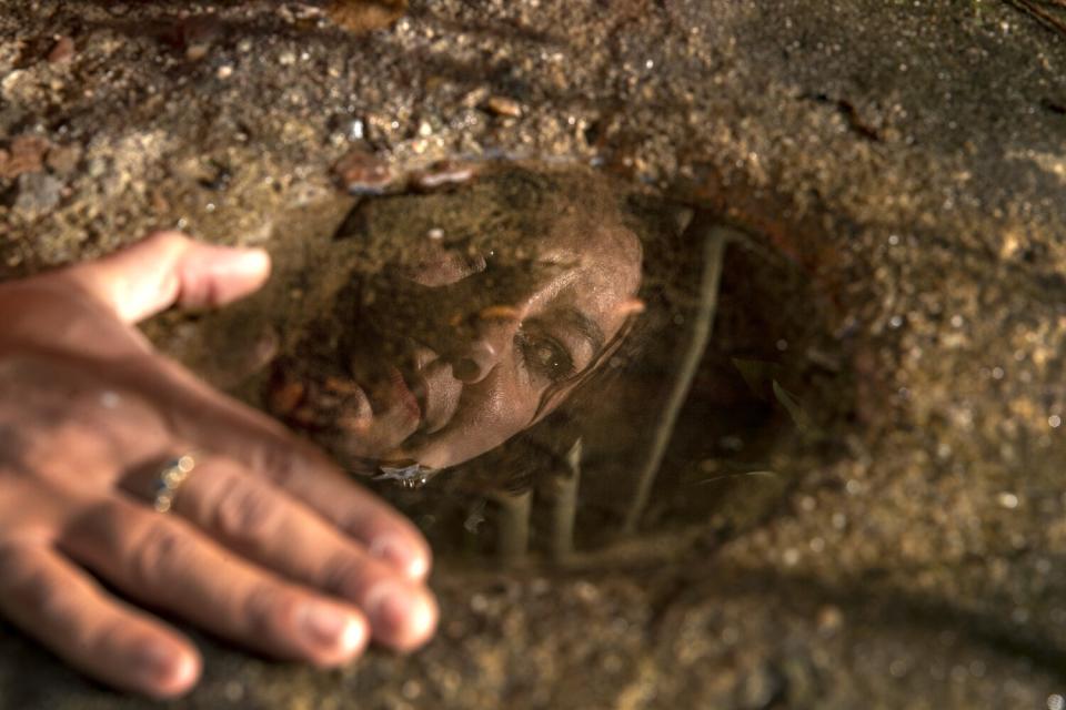 A face is reflected in a pool of water in a bedrock mortar.