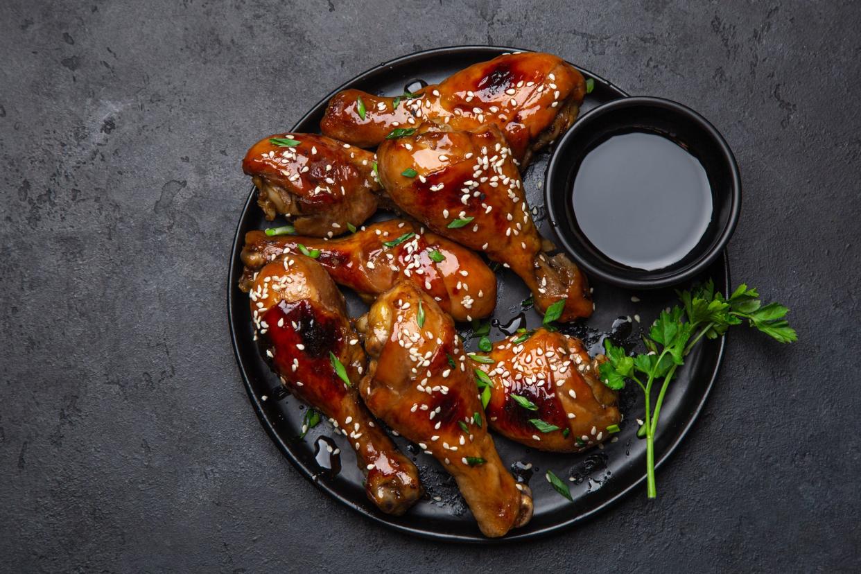 glazed teriyaki chicken legs on black plate, top view, copy space