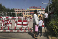 In this Aug. 31, 2018, photo, shot through a car window, a child and a woman wait outside a school entrance with multiple layers of barbed wire and barricades in Peyzawat, western China's Xinjiang region. Uighurs fear the Chinese government's expansion of compulsory Mandarin-intensive classes and boarding schools away from home will gradually erode their children's Central Asian ethnic identity and Islamic beliefs. (AP Photo/Ng Han Guan)