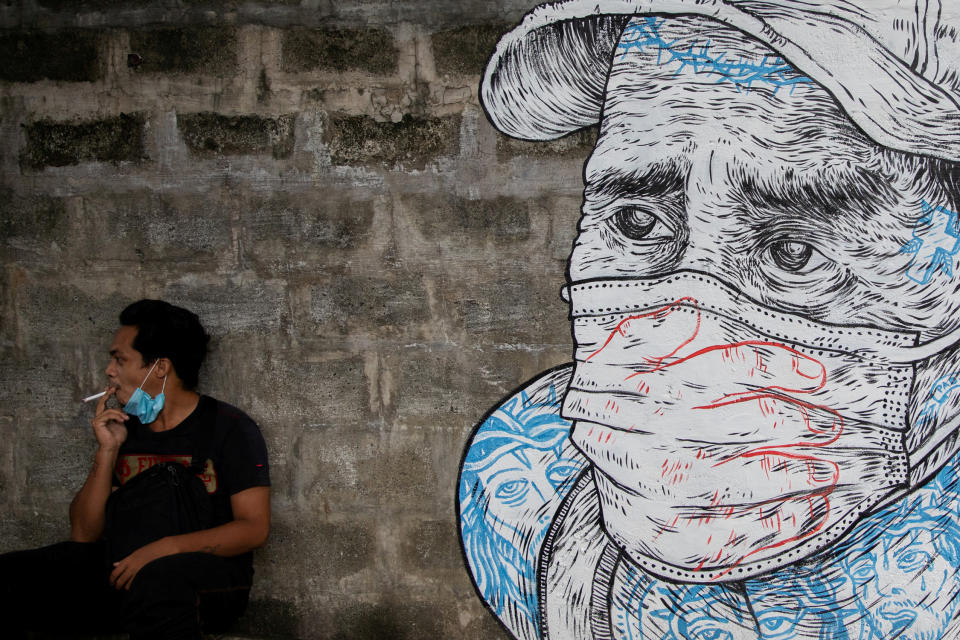 A man smokes a cigarette next to a mural of a man wearing a protective mask amid the coronavirus disease (COVID-19) outbreak in Quezon City, Metro Manila, Philippines, July 30, 2020. REUTERS/Eloisa Lopez