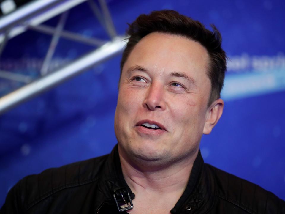 Tesla CEO Elon Musk smiles in front of a blue background