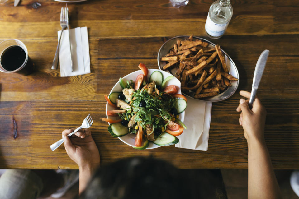 An aerial view of a customer eating salad and fries at a restaurant.