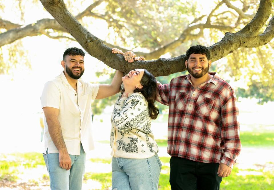 A woman stands between two men under a tree branch in a park