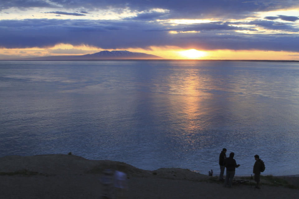 FILE - Visitors to Point Woronzof Park watch the sun set over Cook Inlet and Mount Susitna, also known as Sleeping Lady, on June 7, 2013, in Anchorage, Alaska. Alaska Gov. Mike Dunleavy has proposed a plan that could use the Cook Inlet basin for carbon sequestration. (AP Photo/Dan Joling, File)