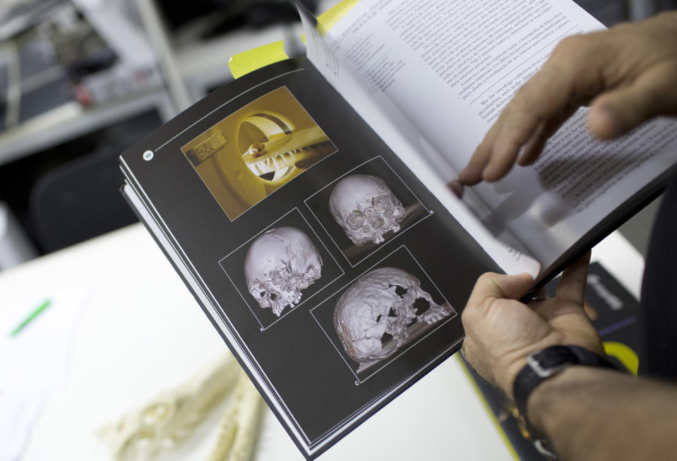 FILE - In this Sept. 5, 2018 file photo, Jorge Lopes, researcher at the Pontifical Catholic University, shows a book with pictures of originals and scanned replicas of some of the artifacts that were inside the National Museum in Rio de Janeiro, Brazil. About 300 pieces of the collection were scanned and some printed in 3D, which could help to rebuild part of the heritage lost in the Sept. 2 fire. (AP Photo/Silvia Izquierdo, File)