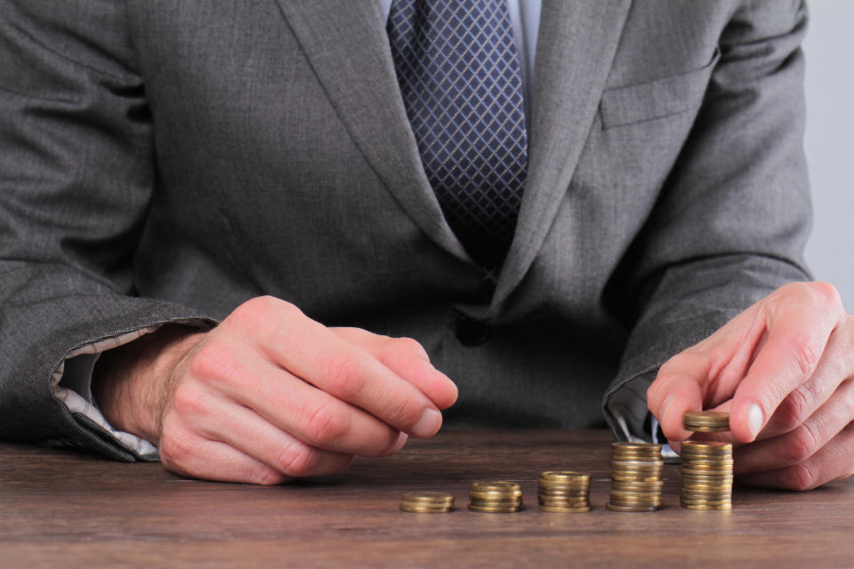 Man in suit stacking successively taller stacks of coins.