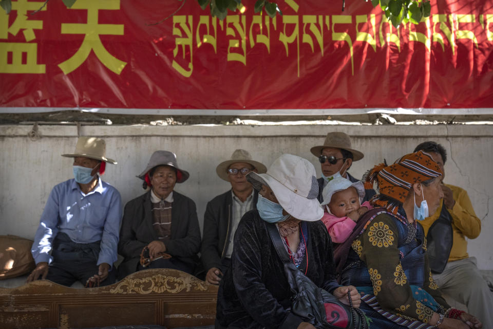 Un grupo de tibetanos se sienta a la sombra de un cartel propagandístico en chino y tibetano cerca de un templo budista del distrito de Chengguan, en Lhasa, la capital de la Región Autónoma Tibetana, el 3 de junio del 2021. (AP Photo/Mark Schiefelbein)