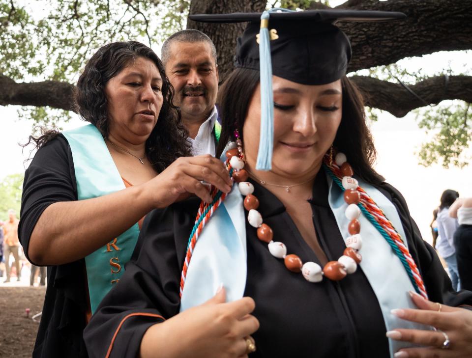 University of Texas graduate Noelia Delgado Rosas gets help with her regalia from her mom, Esthela Delgado Rosas, and dad, Juan Delgado, outside Moody Center on Saturday. Delgado, who earned a Bachelor of Science in kinesiology and health, is a first-generation college graduate and graduated with honors.