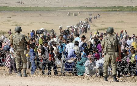 Turkish soldiers stand guard as Syrian Kurds wait behind the border fence to cross into Turkey near the southeastern town of Suruc in Sanliurfa province, September 19, 2014. REUTERS/Stringer