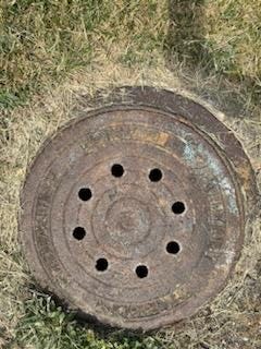 An aged manhole cover was installed before the Metropolitan Sewerage District of Buncombe County introduced newer covers with its logo design in 2010.