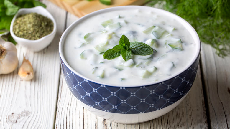 Tzatziki sauce in bowl next to dill and garlic