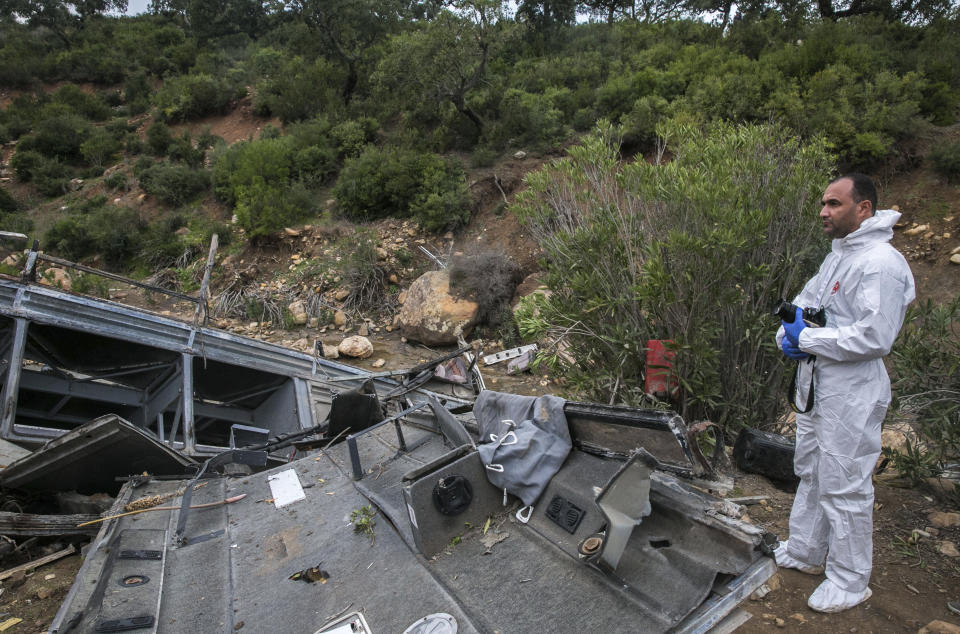 A police investigator stands by a regional bus that crashed off a hill Sunday Dec.1, 2019, killing at least 22 local passengers who were on an excursion in the Amdoun region, northern Tunisia. The bus, which belonged to a private local company, veered of a winding road after the driver failed to maneuver a sharp turn and crashed at the bottom of a ravine. (AP Photo/Riadh Dridi)