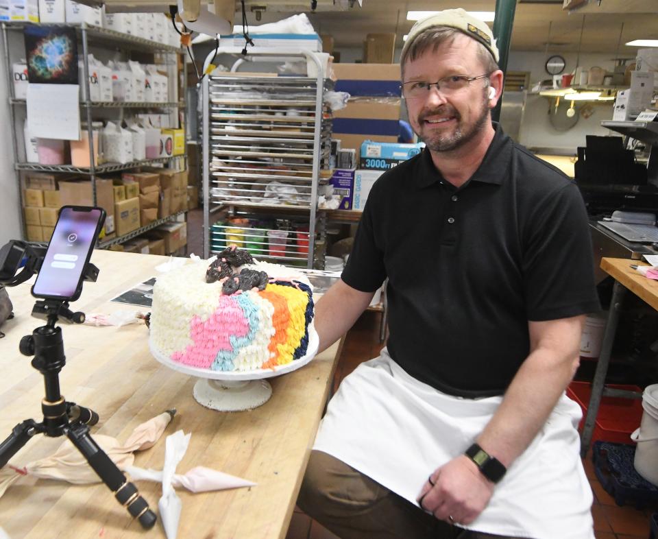 Apple Annie's lead cake decorator Hans Westermark sits next to a cake he decorated at the shop in Wilmington in 2021. Westermark has gained more than 470,000 followers on TikTok for his decorating videos.